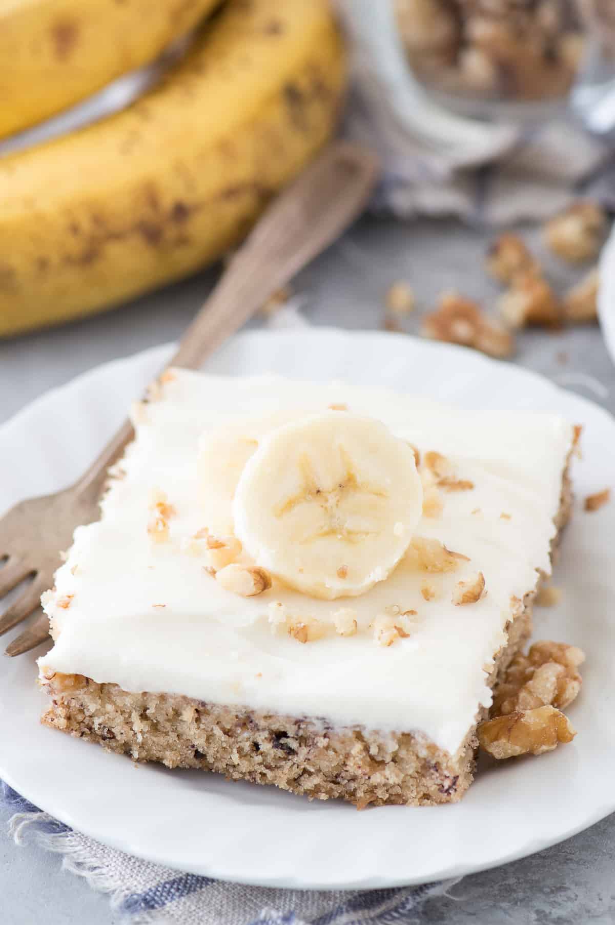 banana bar with cream cheese frosting and banana slice on white plate