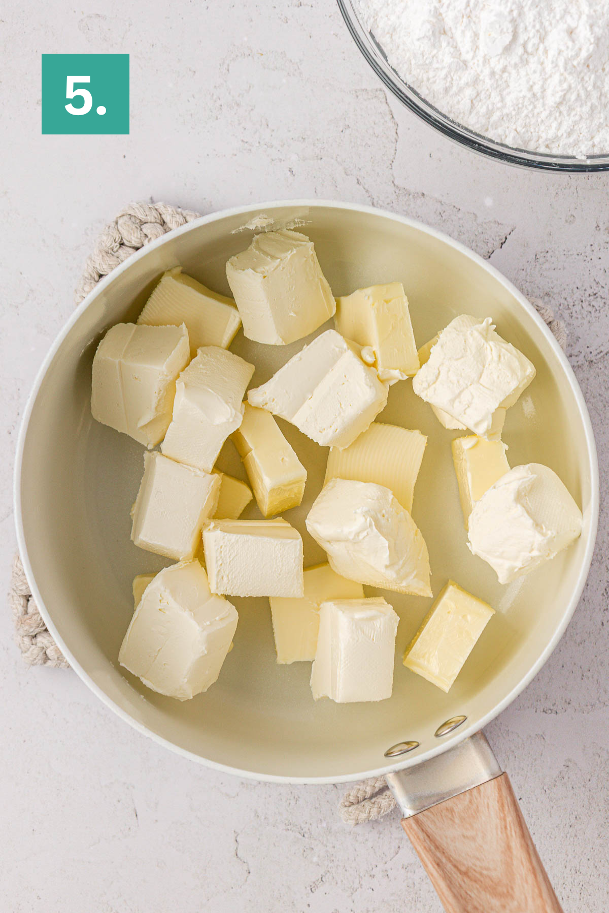 A saucepan filled with cubes of butter and cream cheese, with a bowl of powdered sugar visible in the upper right&mdash;key ingredients for making earthquake cake. The image is labeled with a green box displaying the number 5.