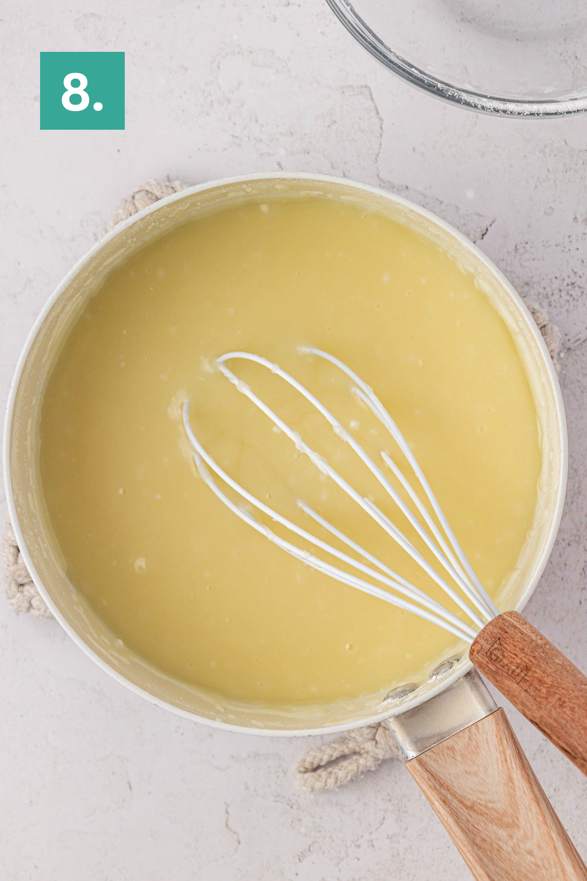 A saucepan filled with smooth yellow batter for an earthquake cake sits on a light surface, with a whisk resting inside. The image is labeled with a green box and the number 8 in the top left corner.