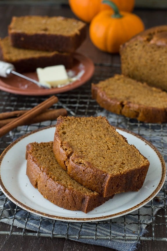 Two slices of pumpkin bread on a small white serving plate on a cooling rack.