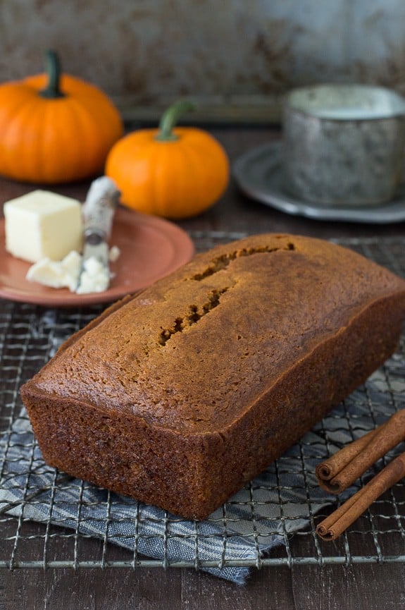 whole pumpkin bread loaf on metal cooling rack with pumpkins in the background