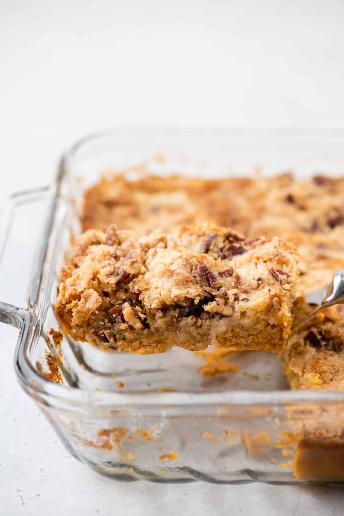 slice of pumpkin dump cake on metal spatula being removed from glass cake pan