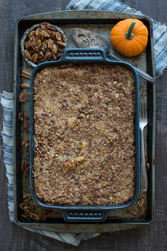 Blue casserole dish with Pumpkin Dump Cake a baking dish surrounded by a small cup of pecans and small pumpkin.