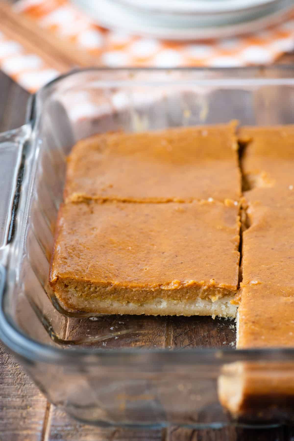pumpkin pie bars in glass baking dish with 1 slice removed on wooden background