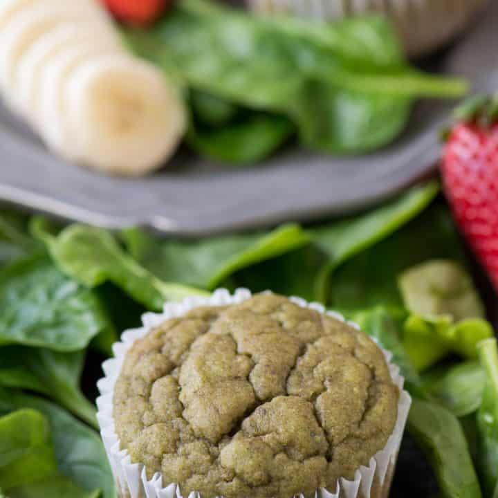 One healthy Green Monster Smoothie Muffin surrounded by spinach on a table.