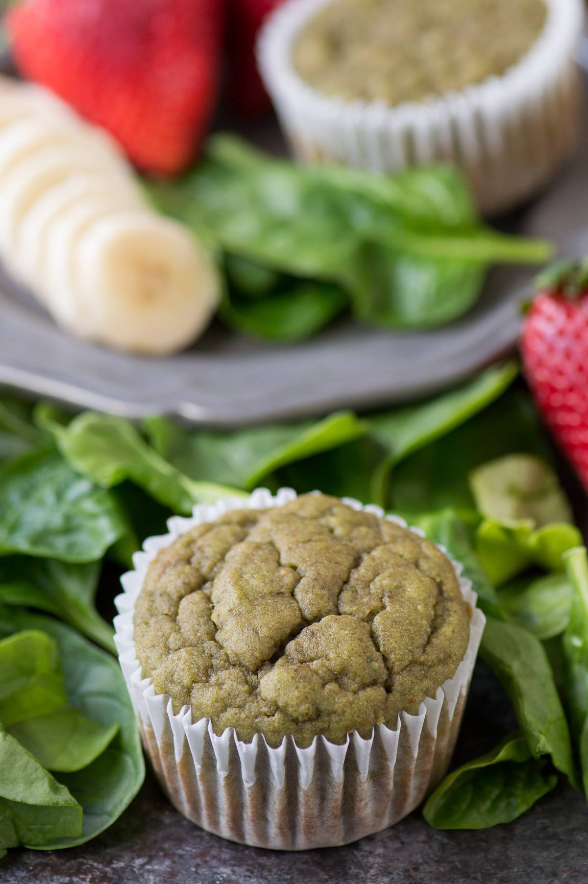 Green Monster Smoothie Muffin surrounded by spinach, bananas and strawberries.