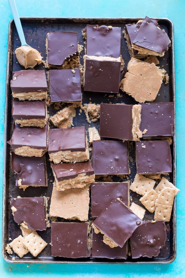 peanut butter bars with chocolate on dark baking sheet on blue background