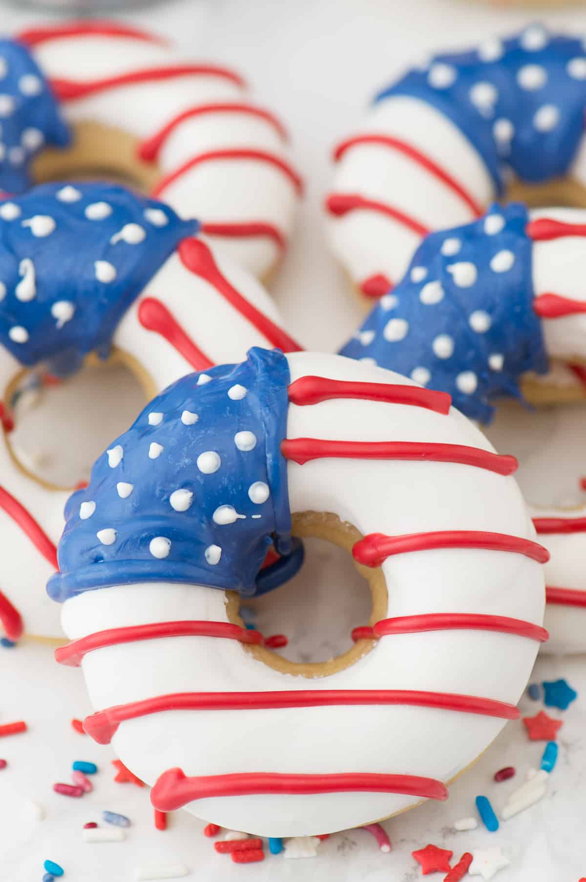 Five homemade American Flag Donuts surrounded by colorful sprinkles.
