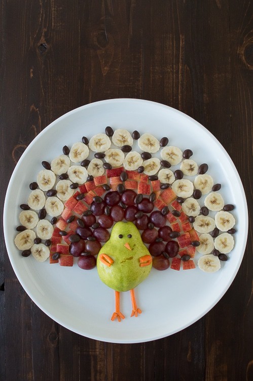Create a healthy fruit platter for Thanksgiving in the shape of a turkey using a pear, grapes, apples, bananas, and chocolate covered raisins! 