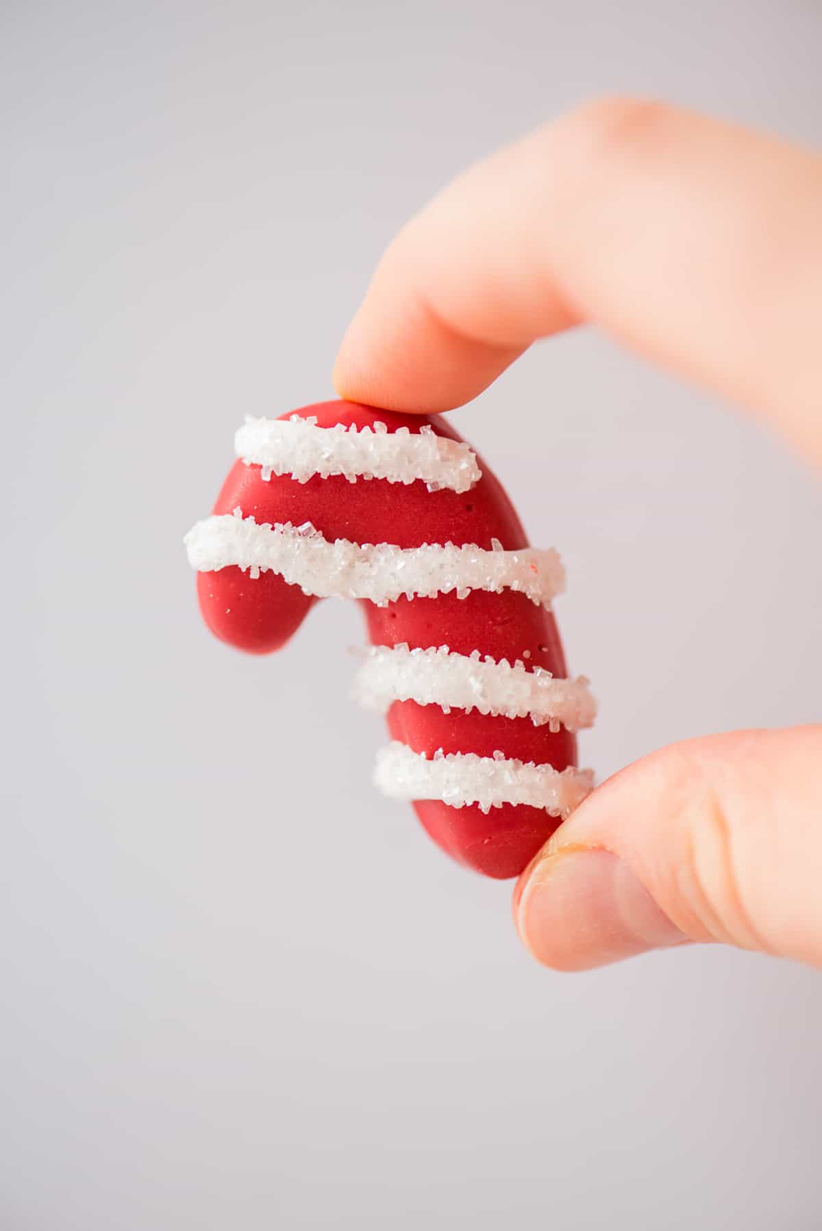 fingers holding a candy cane shaped oreo ball on white background