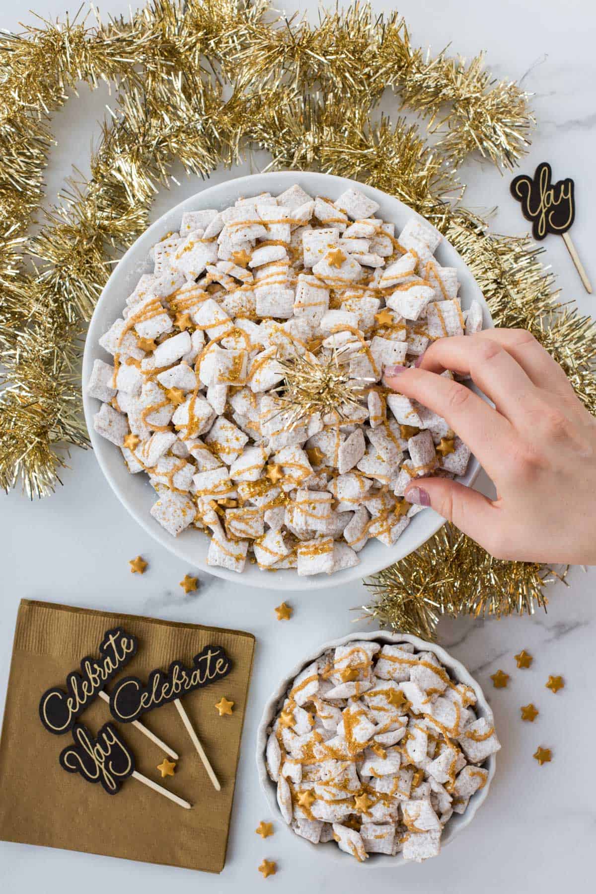 new year’s eve white chocolate puppy chow with gold sprinkles and gold stars on a white background 