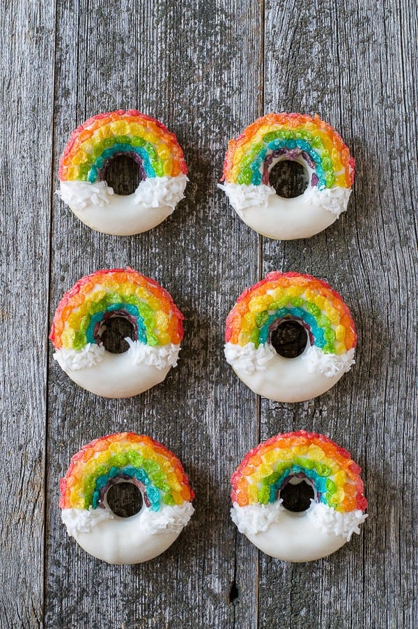 Six homemade Rainbow Donuts on a wooden table.
