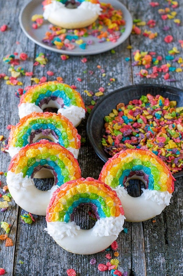 Rainbow Donuts with white chocolate, coconut shavings and fruity pebbles on a wooden table.