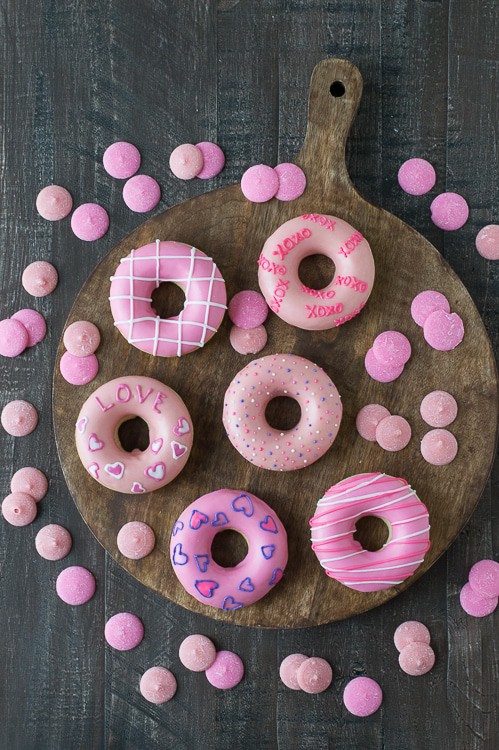 Delicious and cute Pink Valentine’s Day Donuts on a wooden board surrounded by pink candy melts. 