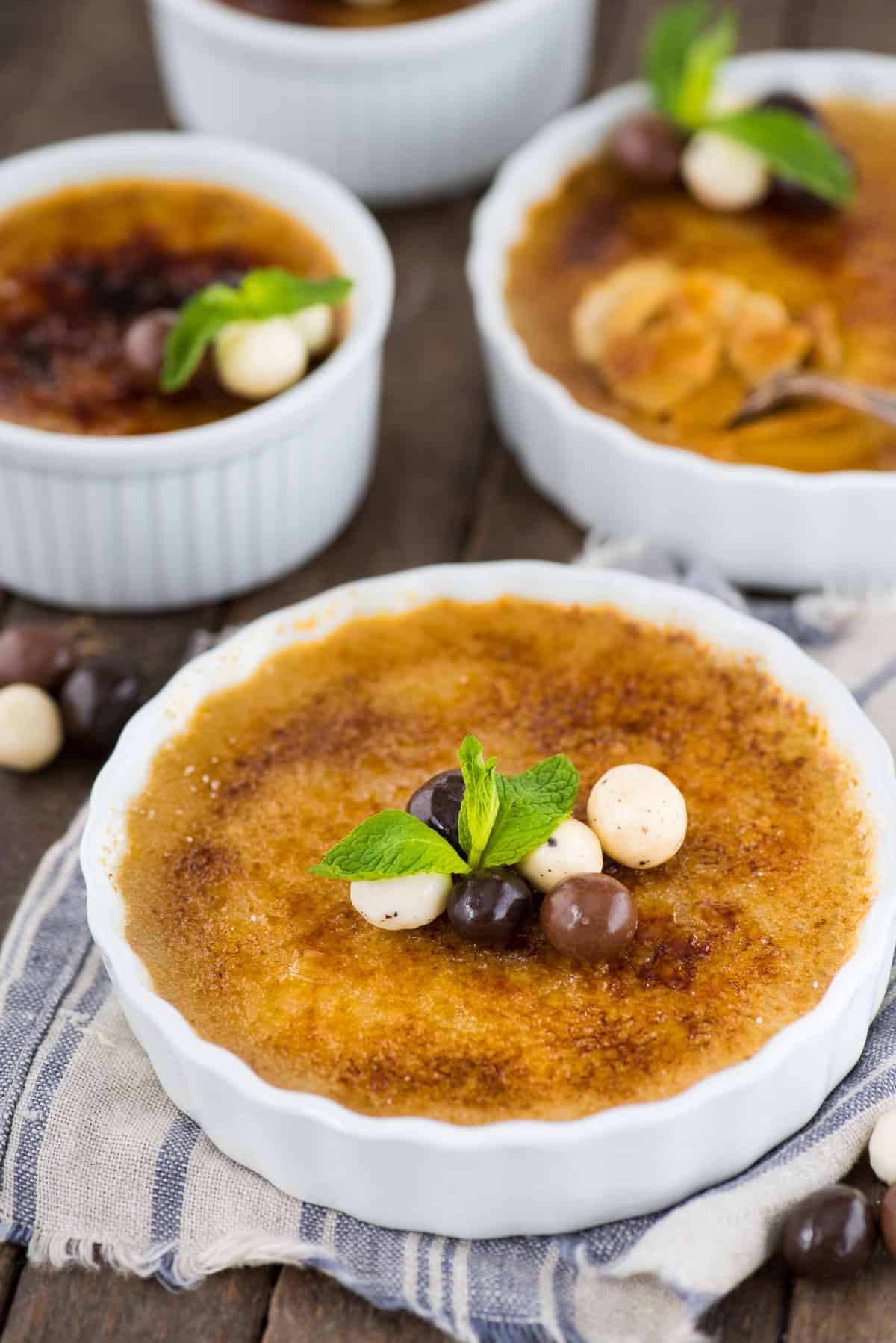 espresso creme brûlée in white round ramekin with chocolate covered coffee beans and mint leaf on top of creme brûlée