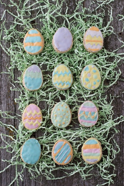 Twelve Rice Krispies Easter Egg treats on fake green grass on top of a wooden table.