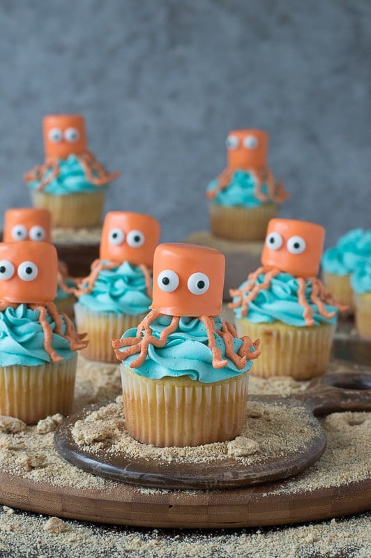 Seven orange and blue Octopus Cupcakes on a wooden board.