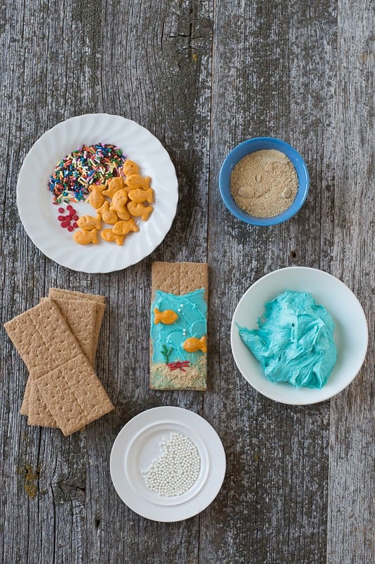Under the Sea Graham Crackers Ingredients - multi colored sprinkles, graham crackers and blue buttercream on a wooden table.
