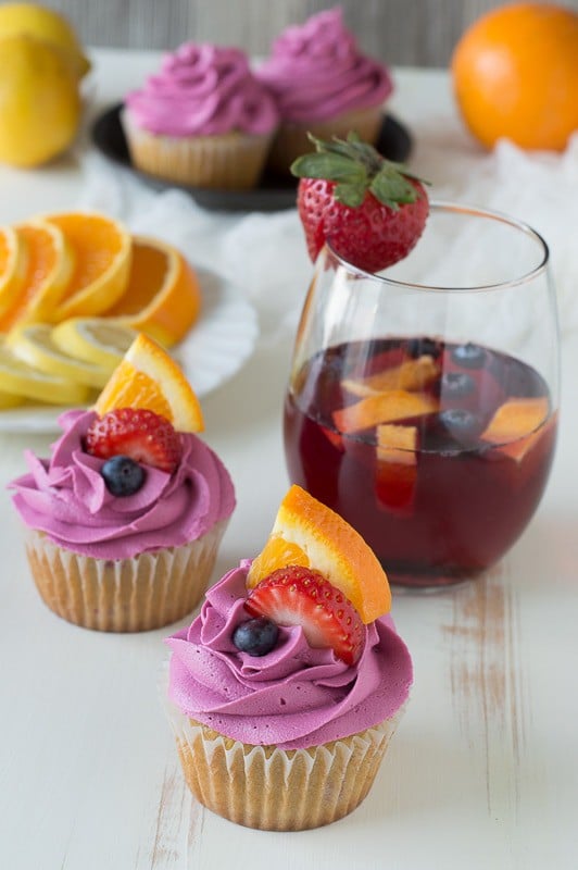 Two delicious Sangria Cupcakes garnished with fresh blueberries, strawberries and a slice of orange.