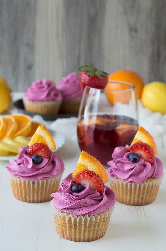 Three delicious Sangria Cupcakes with red wine frosting and fresh blueberries, strawberries and sliced oranges. 