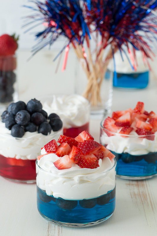blue jello in glass cup topped with whipped cream and chopped strawberries 
