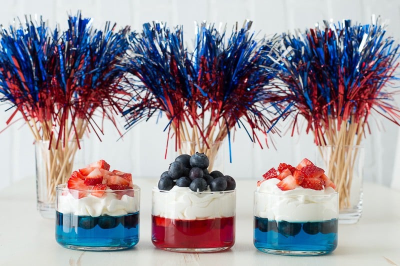 blue and red jello in glass cups topped with whipped cream and chopped strawberries and blueberries