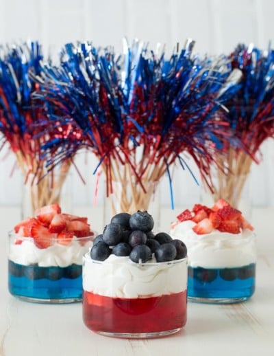 A table of Memorial Day desserts featuring a flag cake, red, white, and blue fruit parfaits, and star-shaped cookies.