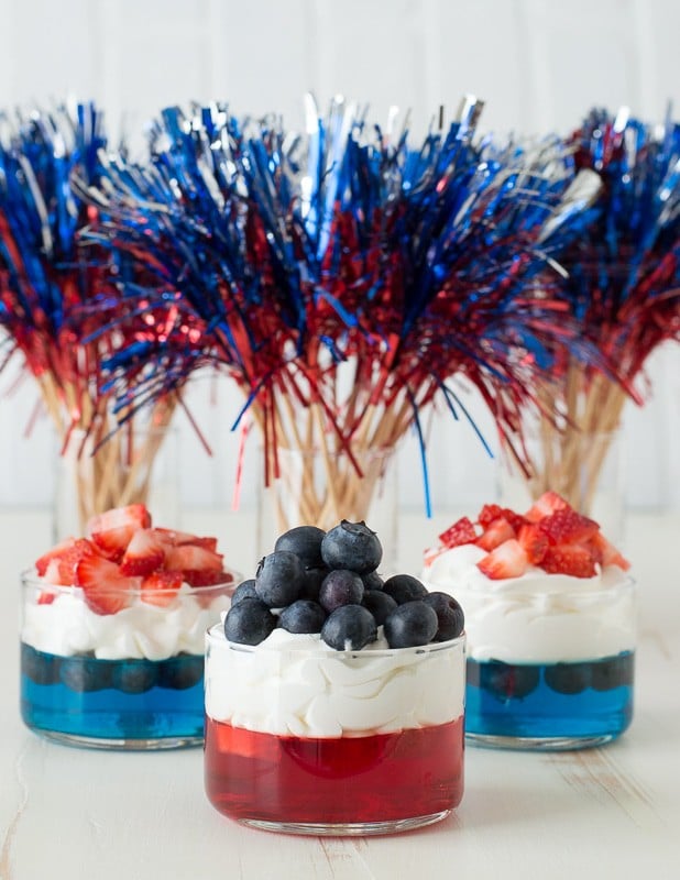 blue and red jello in glass cups topped with whipped cream and chopped strawberries and blueberries