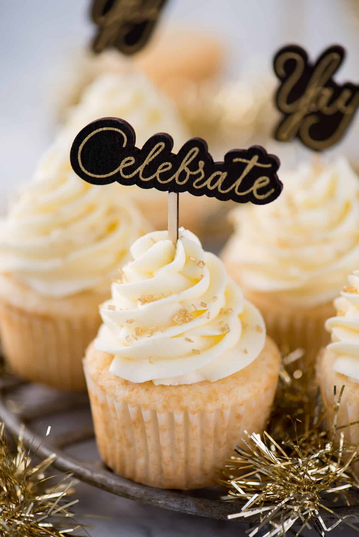 easy champagne cupcakes with champagne buttercream topped with gold sprinkles and a cupcake topper that says "celebrate"