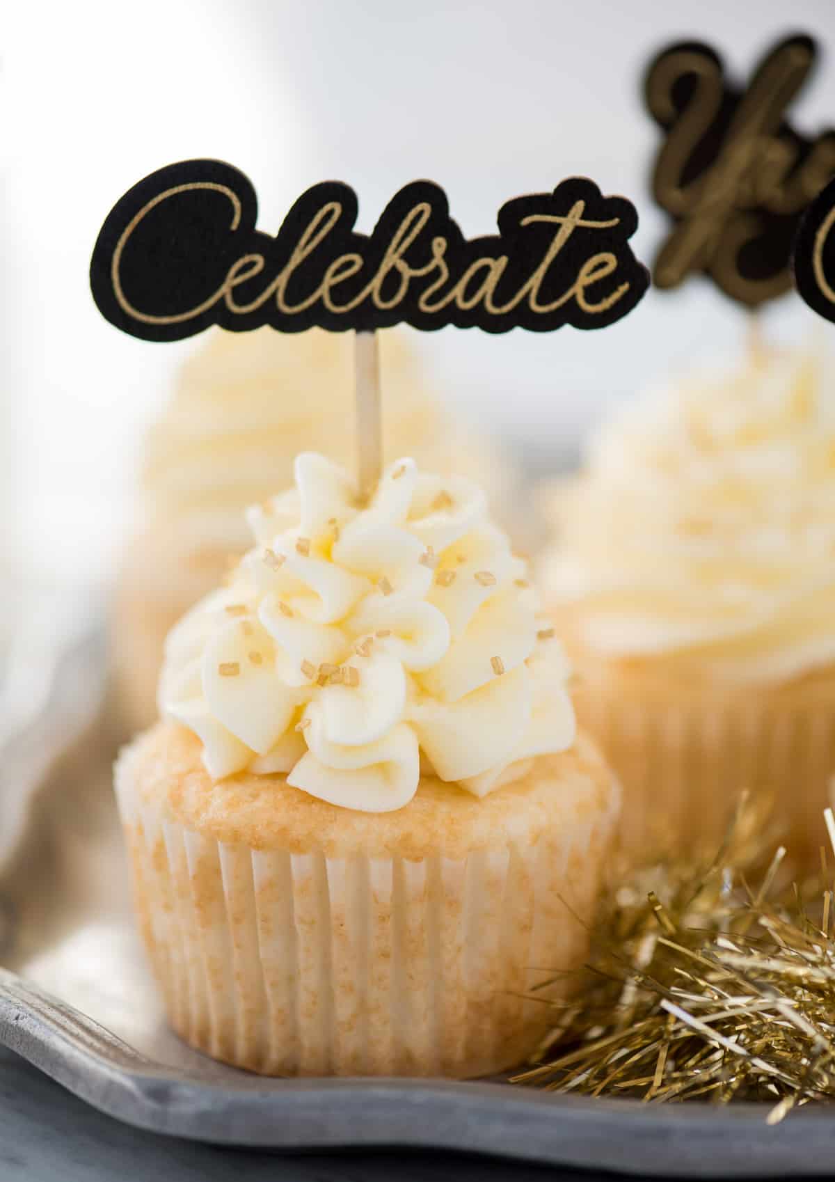 easy champagne cupcakes with champagne buttercream topped with gold sprinkles and a cupcake topper that says "celebrate"