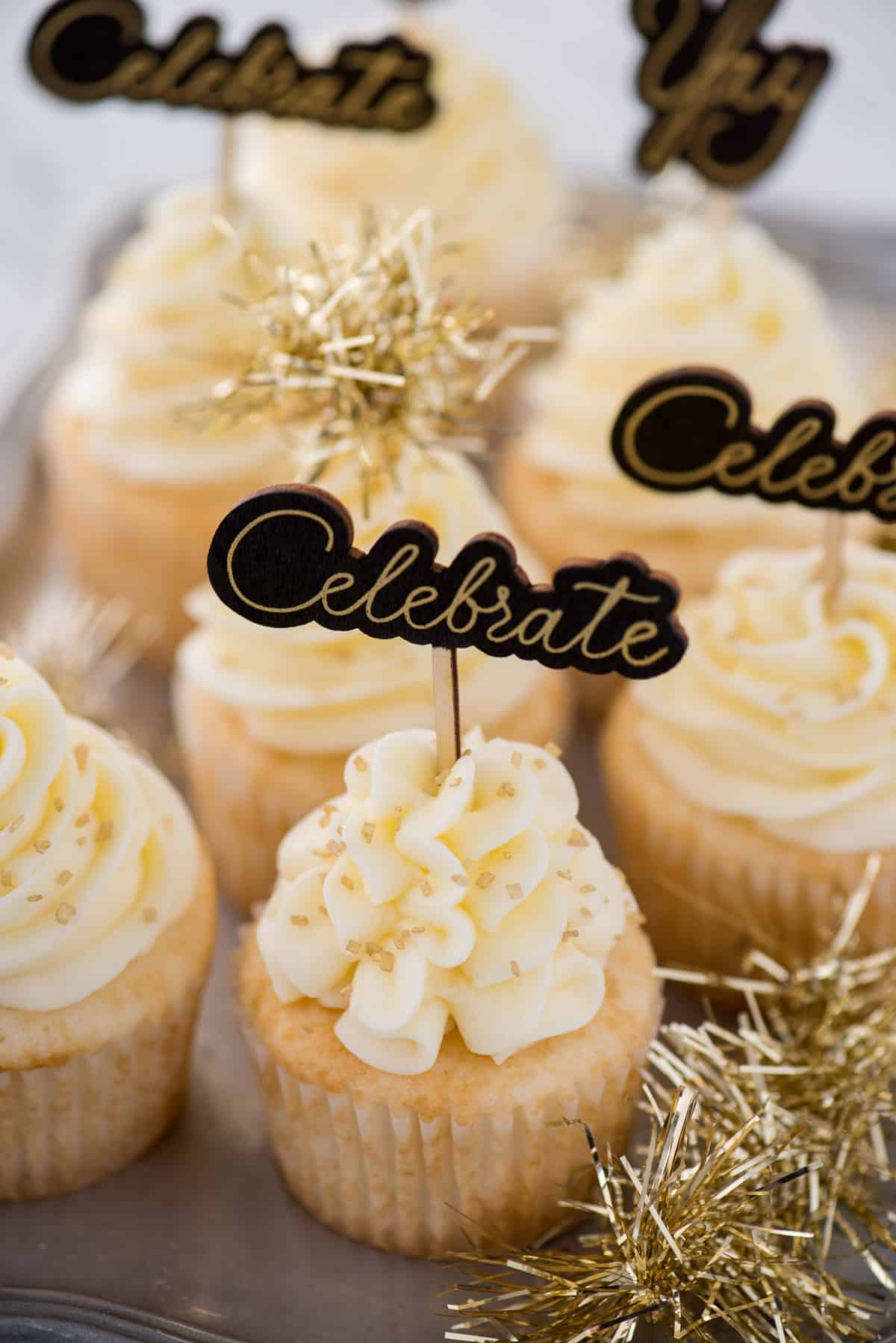 easy champagne cupcakes with champagne buttercream topped with gold sprinkles and a cupcake topper that says "celebrate"