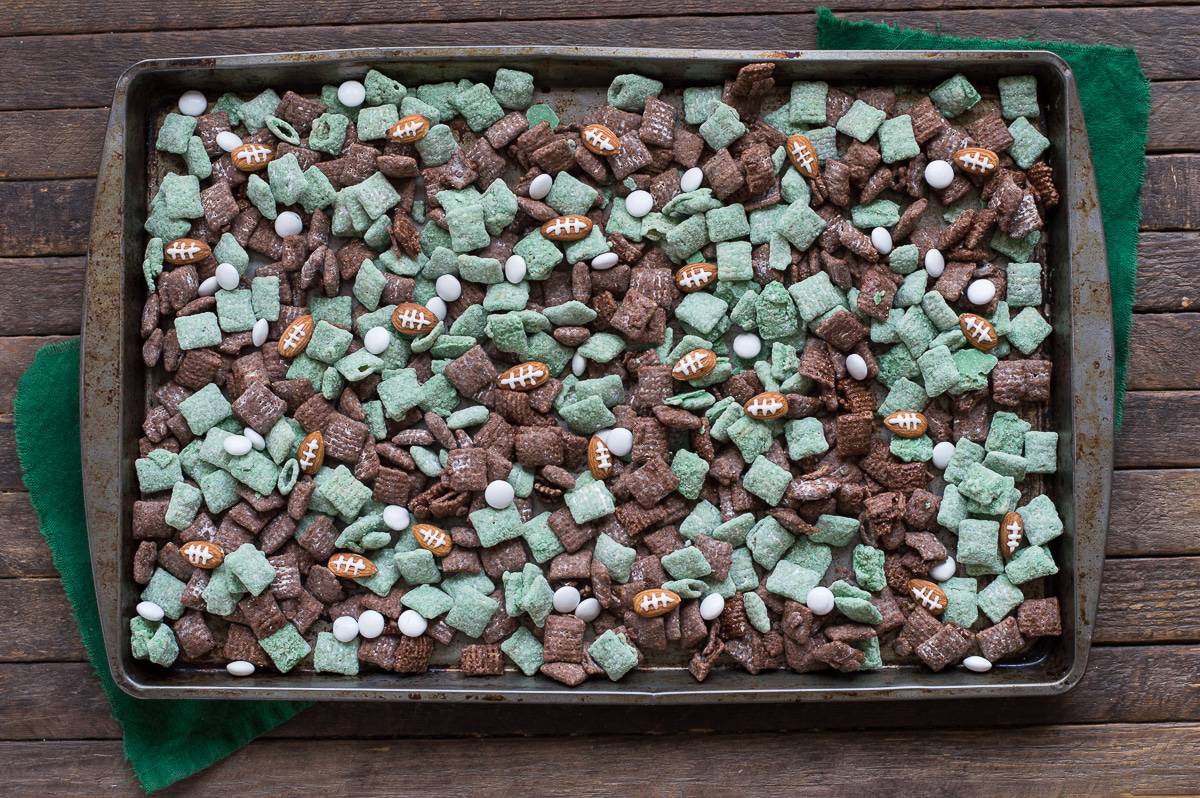 green and brown Football Puppy Chow with almonds that look like footballs and Game Day Flags on baking sheet