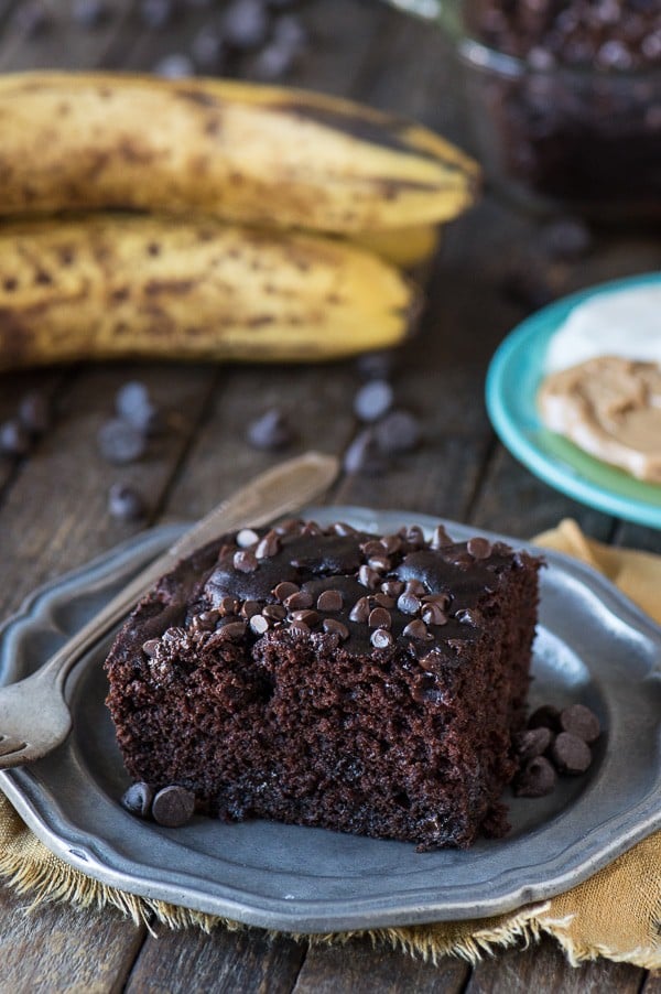 slice of healthier chocolate cake on metal plate with banana in the background
