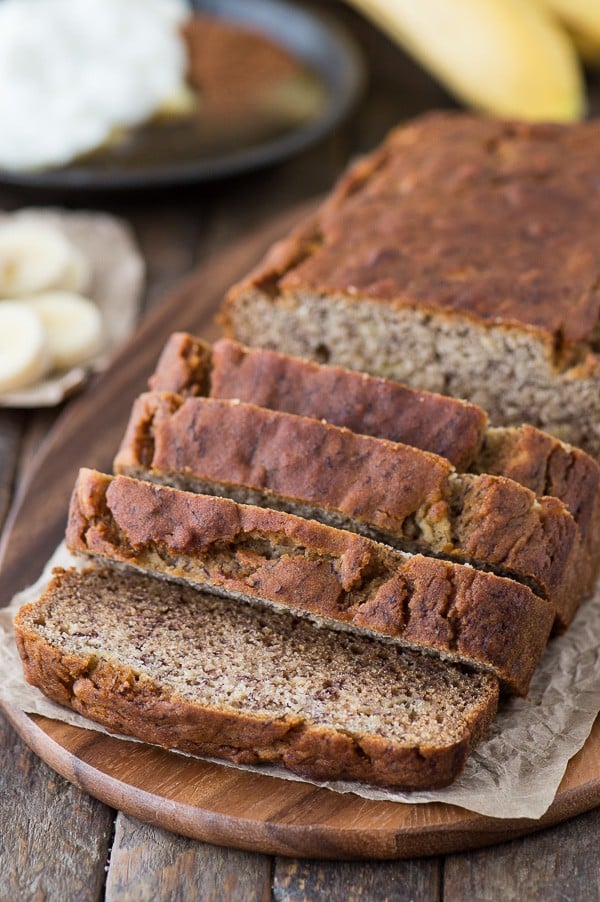 Healthier banana bread sliced on wood platter.