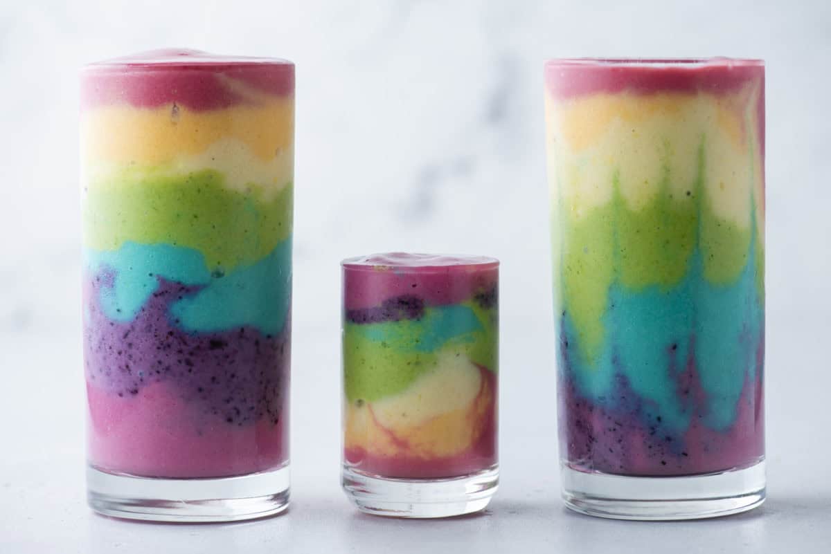 3 rainbow smoothies in glass cups on a white background