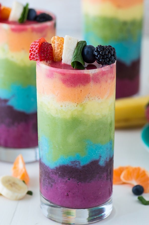 Rainbow Smoothie |in a clear glass garnished with blueberries, raspberries, oranges and bananas.