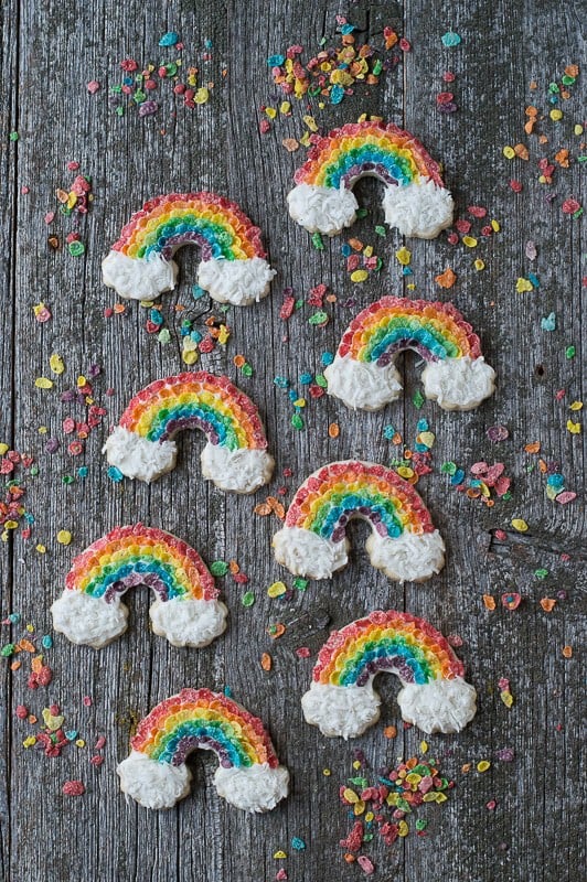 Eight Rainbow Sugar Cookies surrounded by fruity pebbles on a wooden table.