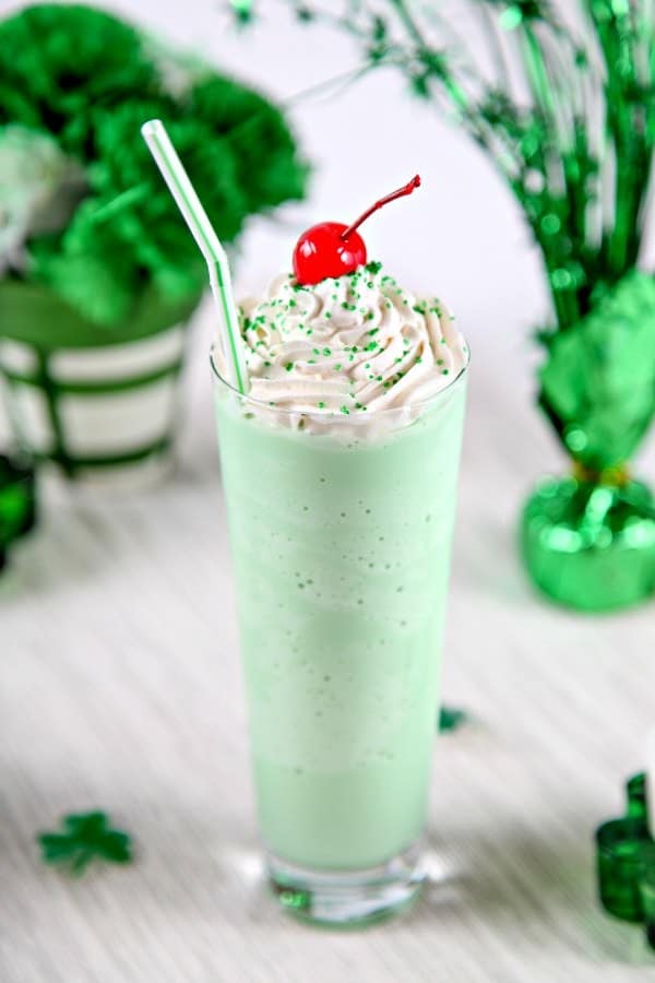 Homemade Shamrock Shake in a clear glass cup with a cherry on top and a white and green straw.