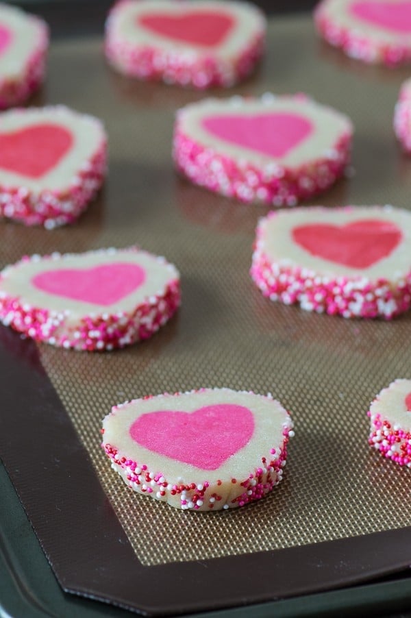 Ten Easy Homemade Valentine’s Day Slice N’ Bake Cookies covered in pink and white sprinkles on a baking sheet.
