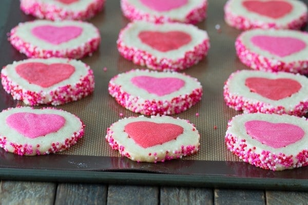 Pink Homemade Valentine’s Day Cookies on a baking sheet on top of a wooden table. 