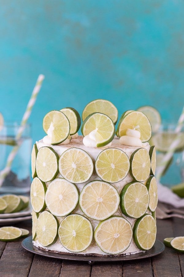 Coconut Lime Cake covered in sliced lime on a cake platter on a wooden table.