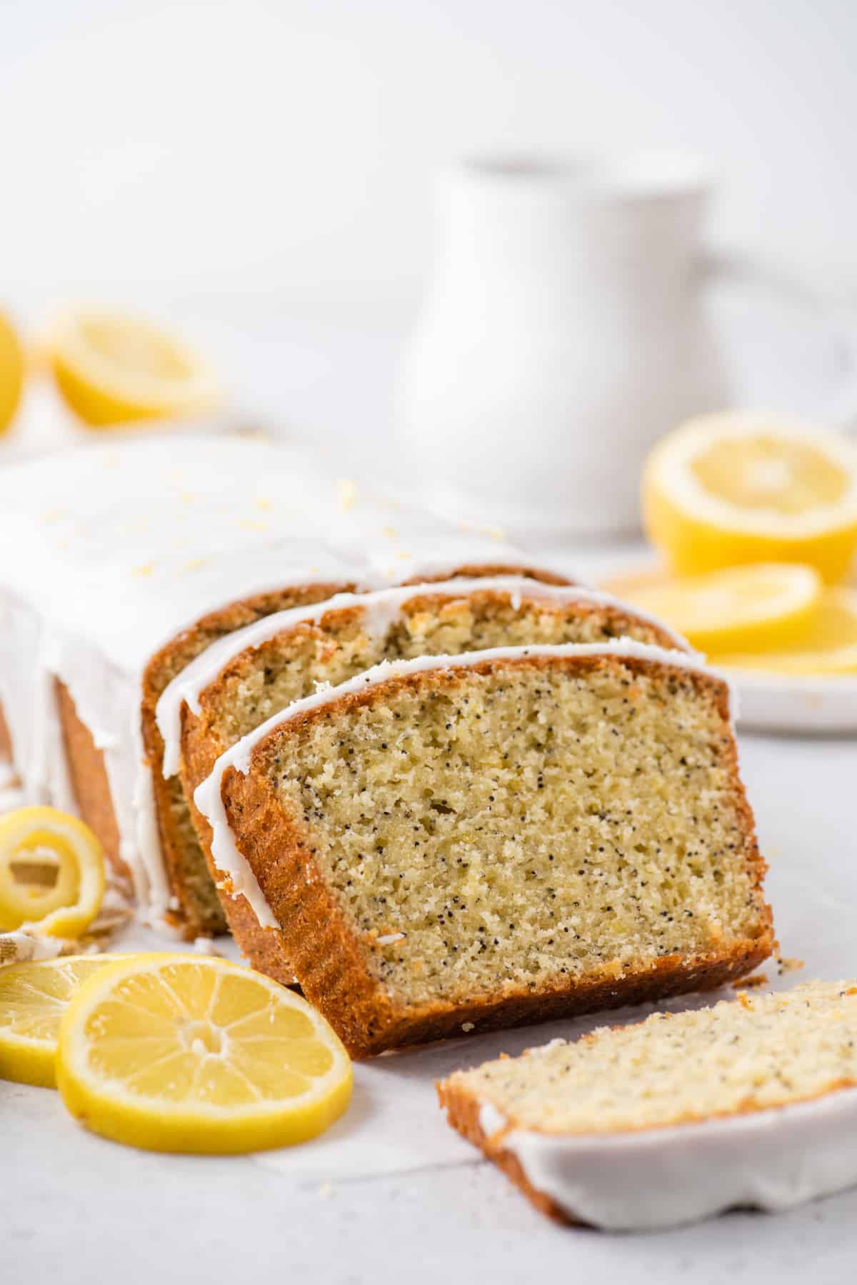 Sliced lemon poppy seed bread with slices of lemons and white pitcher in background