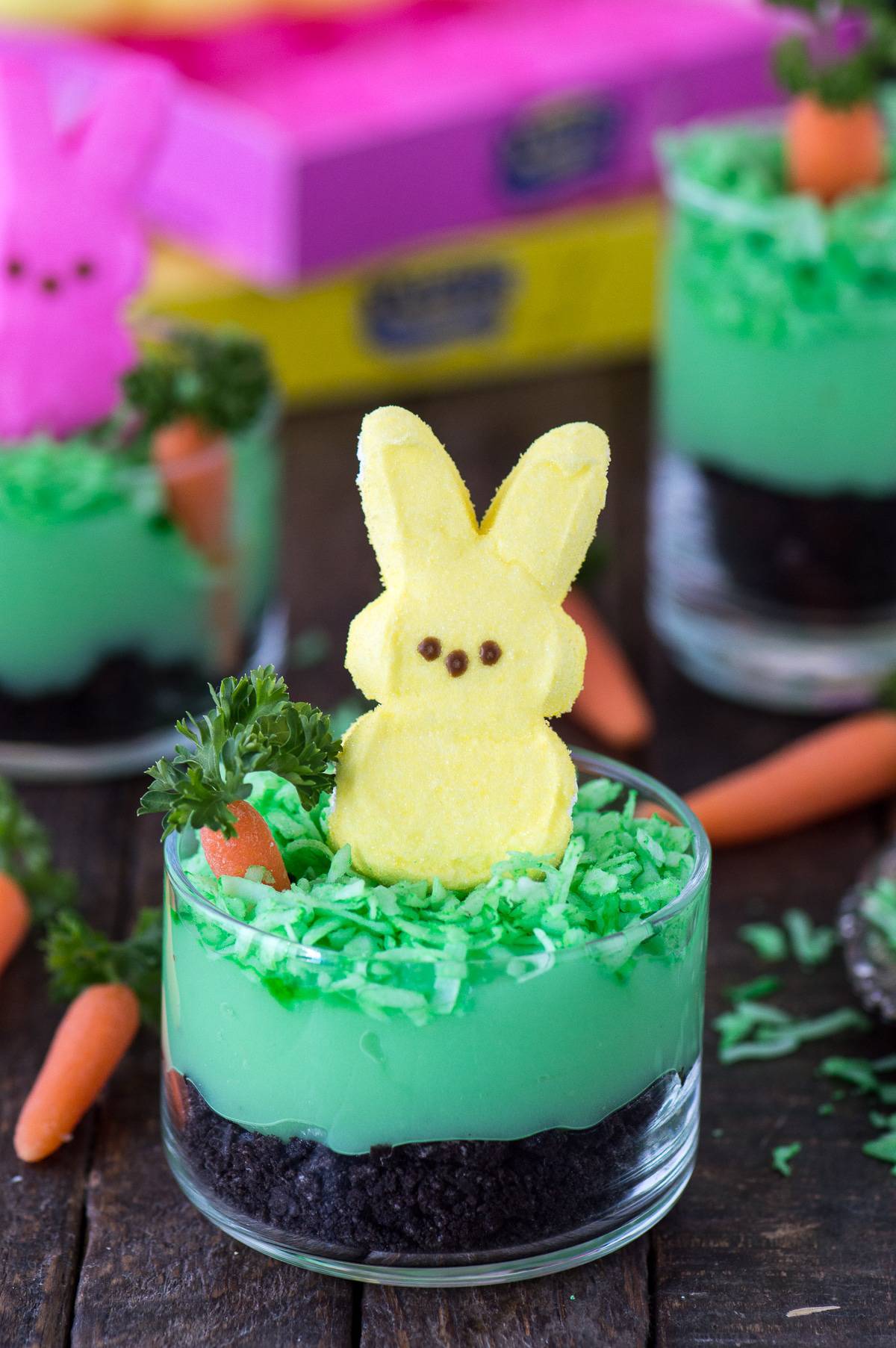 Peeps bunny pudding dirt cups with oreos, pudding, coconut, a mini carrot and a peep in a glass dessert bowl