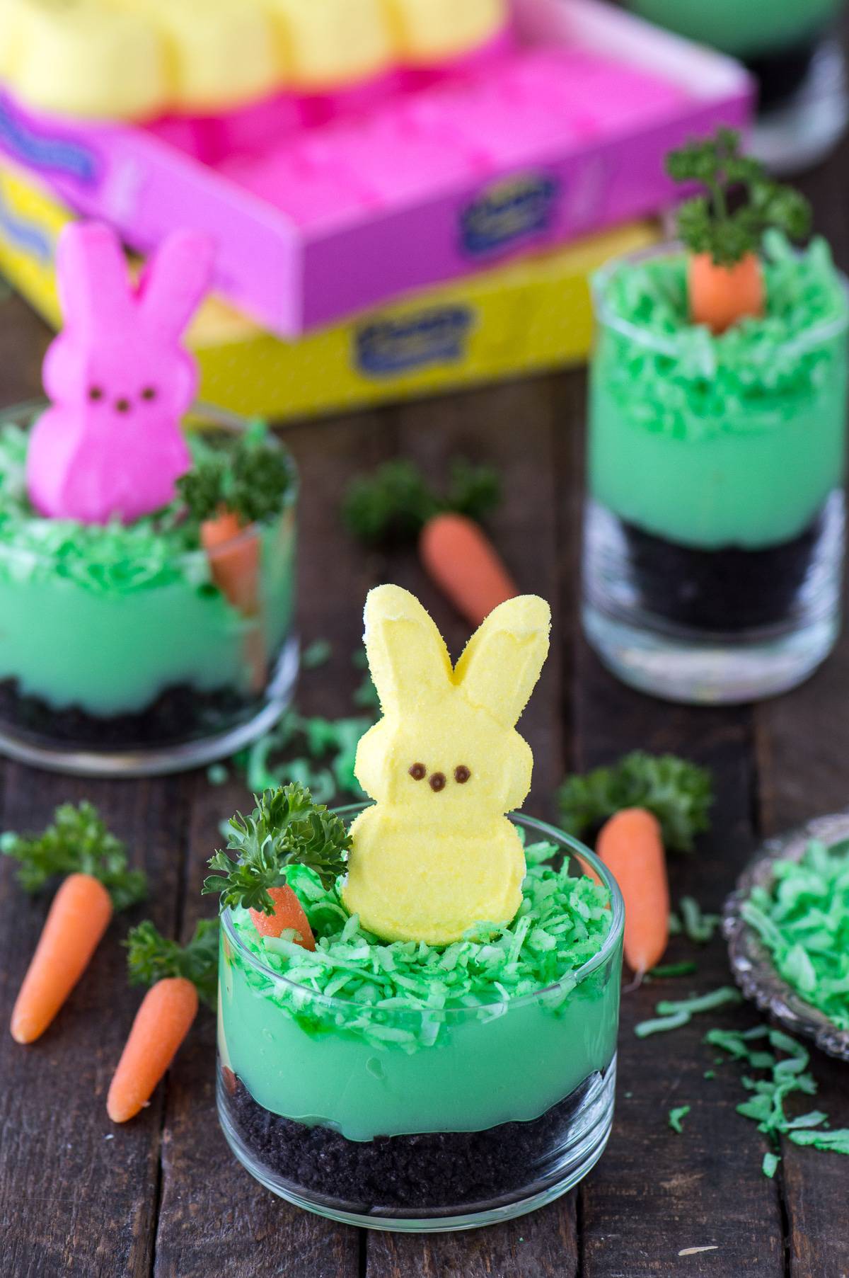 Peeps bunny pudding dirt cups with oreos, pudding, coconut, a mini carrot and a peep in a glass dessert bowl