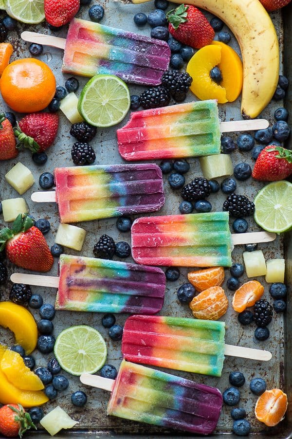 rainbow popsicles on platter with blueberries, bananas, oranges, limes, strawberries surrounding the popsicles