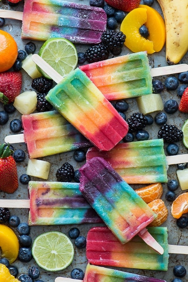 rainbow popsicles on platter with blueberries, bananas, oranges, limes, strawberries surrounding the popsicles.