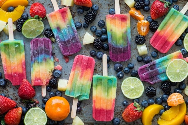 rainbow popsicles on platter with blueberries, bananas, oranges, limes, strawberries surrounding the popsicles.