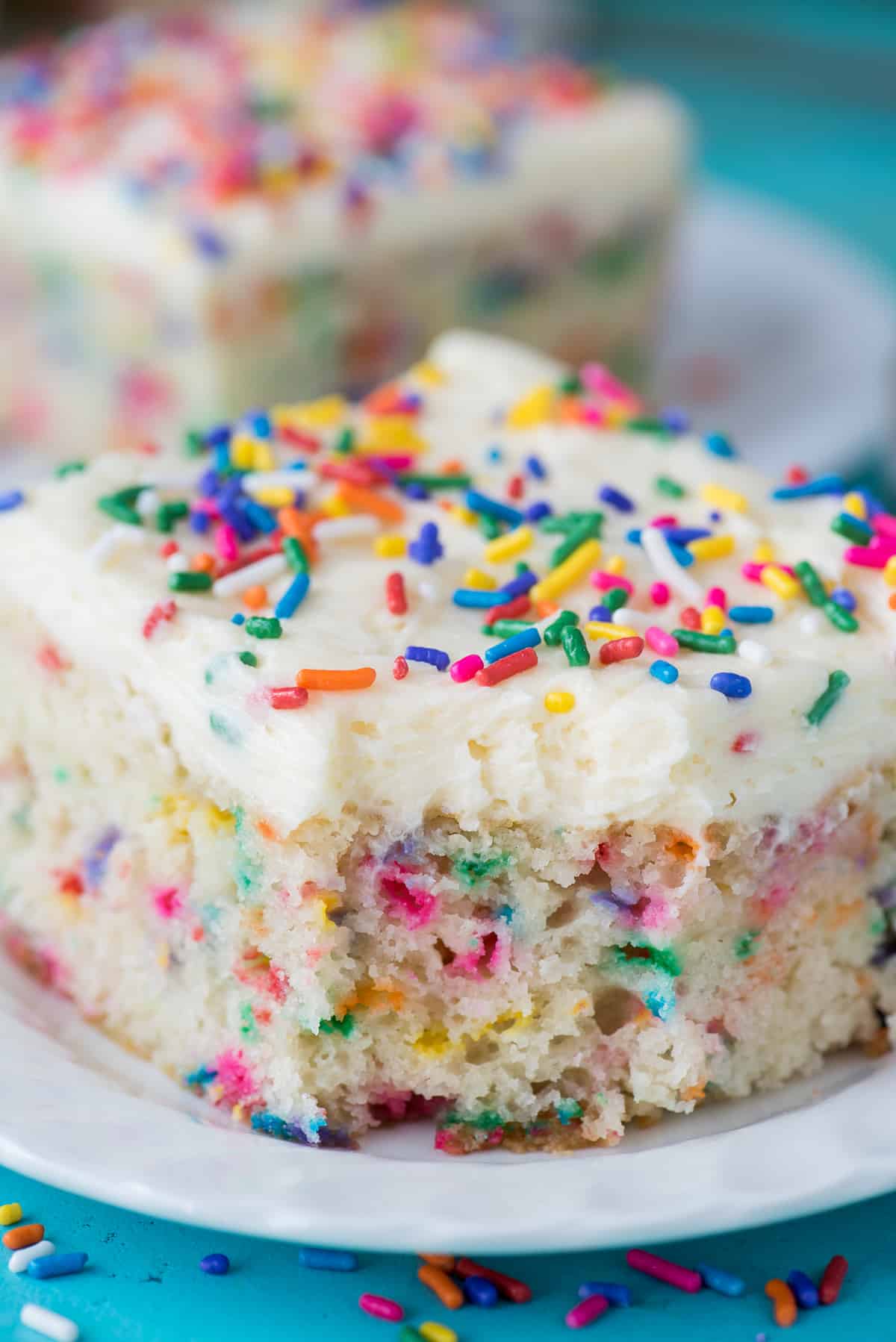 piece of funfetti cake with bite removed on white plate on teal background