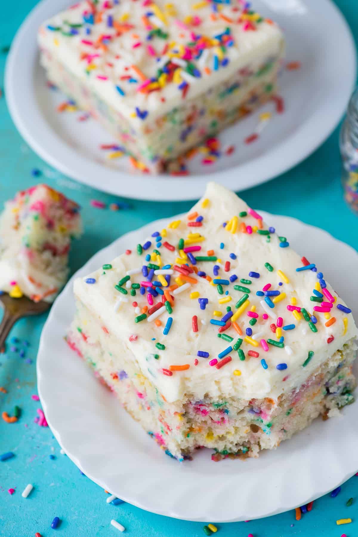 two pieces of funfetti cake on white plates on teal background