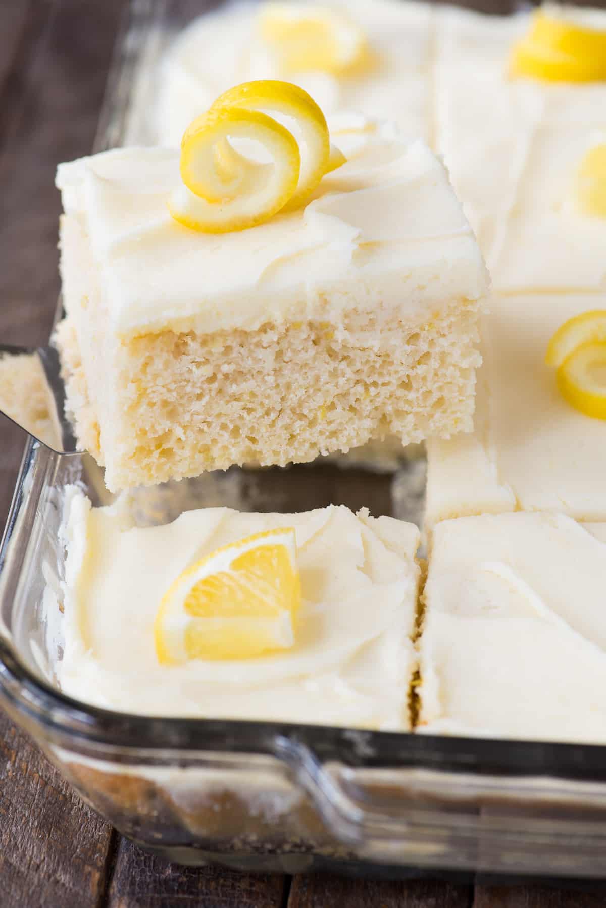 piece of lemon cake with white frosting and lemon peel on top on metal spatula